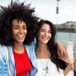 Two digital nomad women smiling at the camera along the waterfront.