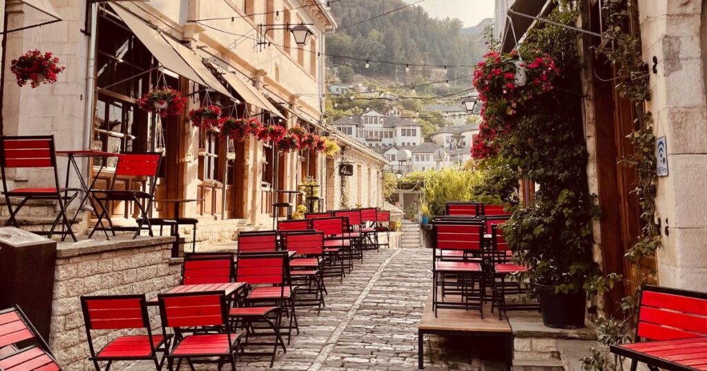 Cobblestone street in Albania lined with red chairs and hanging flowerpots