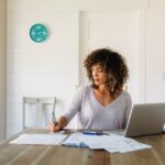 US small business owner sits at a table in a kitchen claiming her self employment tax deductions.