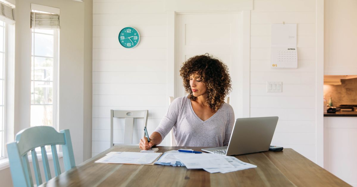 US small business owner sits at a table in a kitchen claiming her self employment tax deductions.