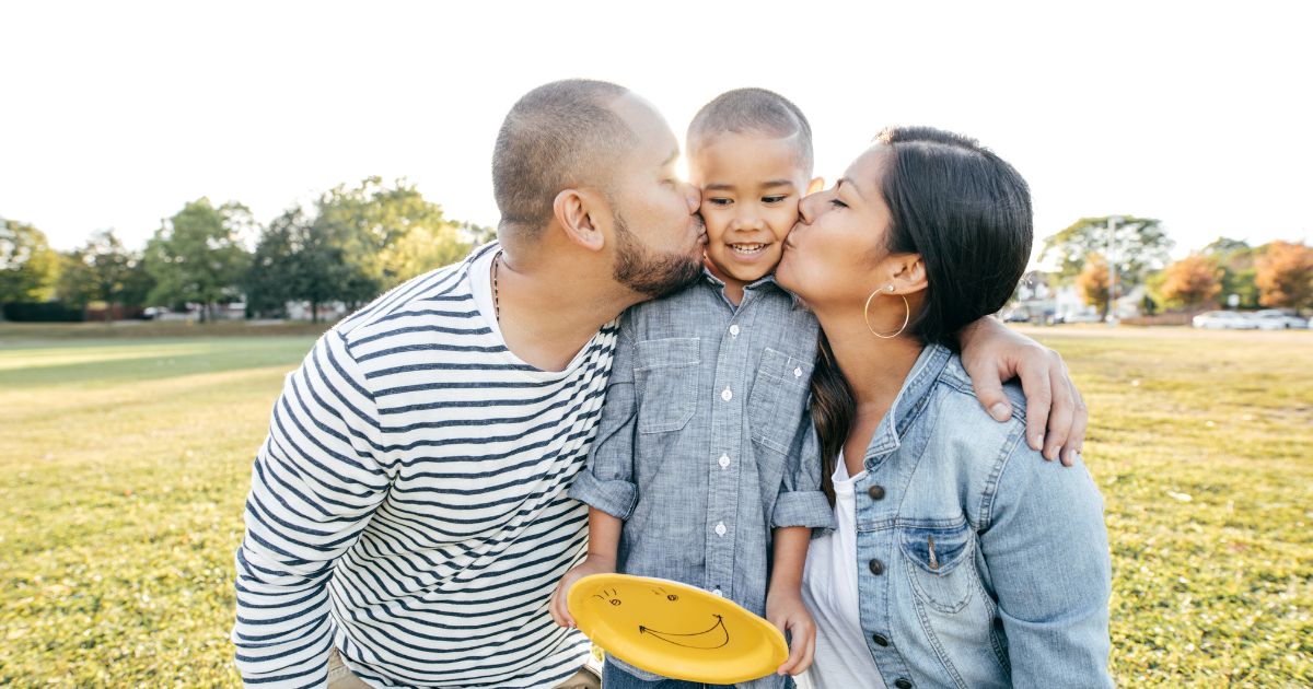 US parents kiss their child while spending time outside together.