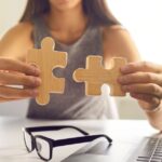 Woman holds two pieces of a jigsaw puzzle together, representing how FBAR vs 8938 apply to US expat taxes.